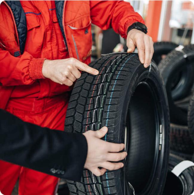 A mechanic in red overalls points to the tread of a new winter tire.