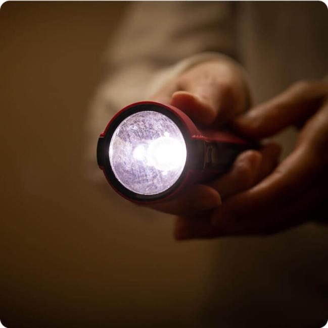 A person holds a lit flashlight, illuminating a dark room.