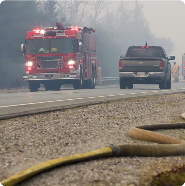 A red fire truck with flashing lights drives down a smoky road.